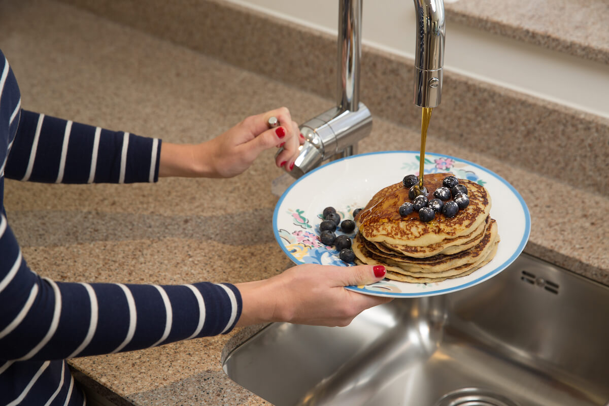 close up of woman using maple tap over pancakes